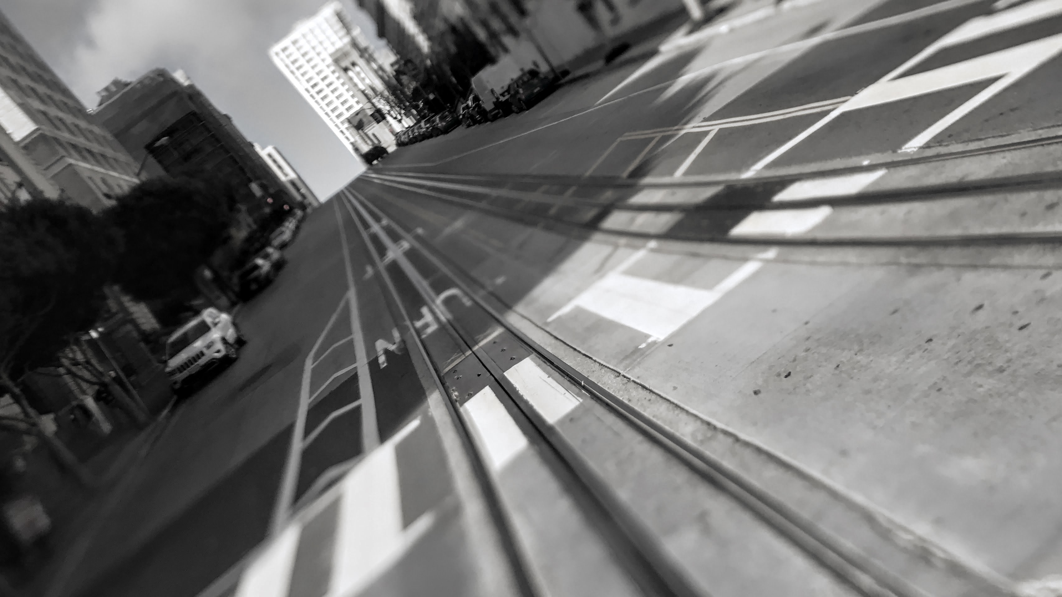 Tilted, partially blurred, clack and white image of a street with embedded tracks that converge on the horizon.